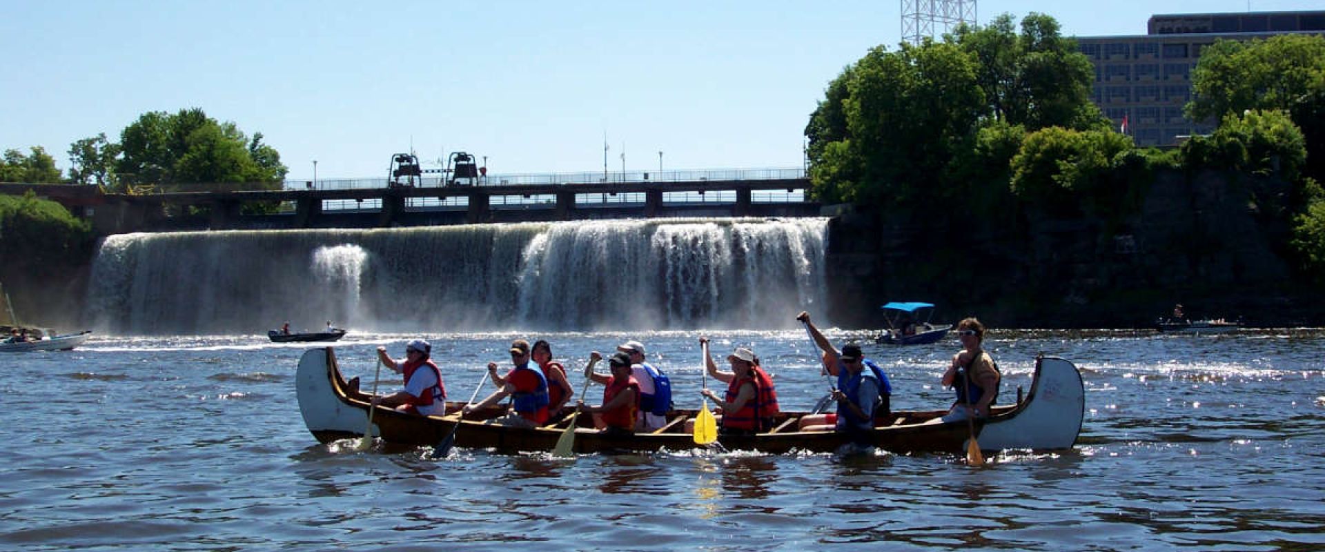 A group of paddlers canoe past Rideau Falls on the Ottawa River on Canadian Rivers Day
